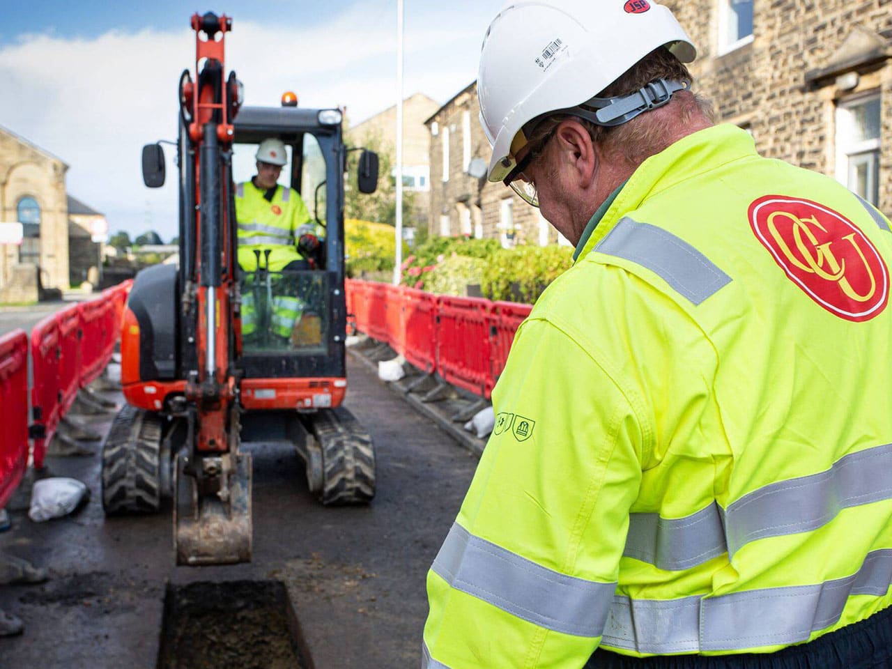 OCU Group engineer in hi-vis beside a mini digger on a street works site
