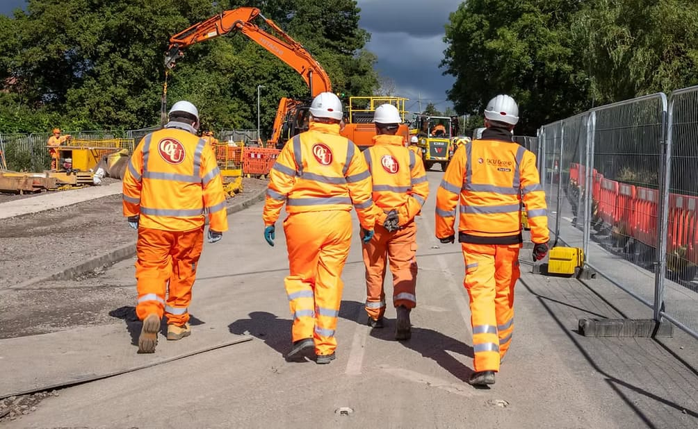Four OCU Group engineers in orange hi-vis walking along a roadworks site