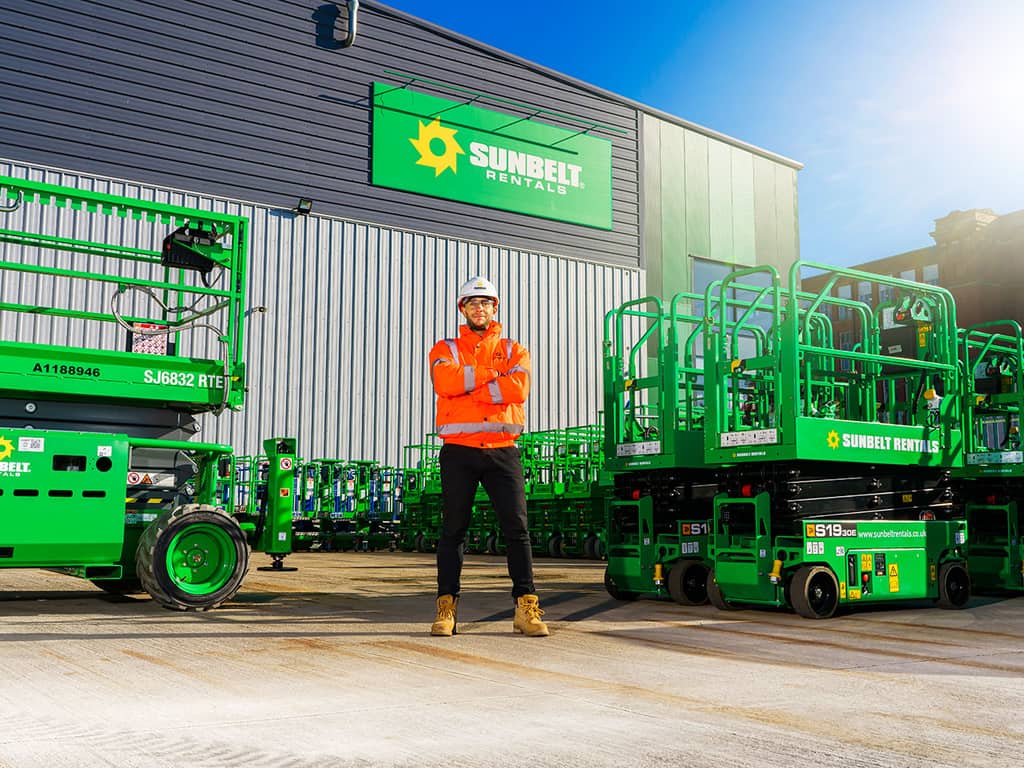 Sunbelt Rentals worker standing among green access platforms outside a depot