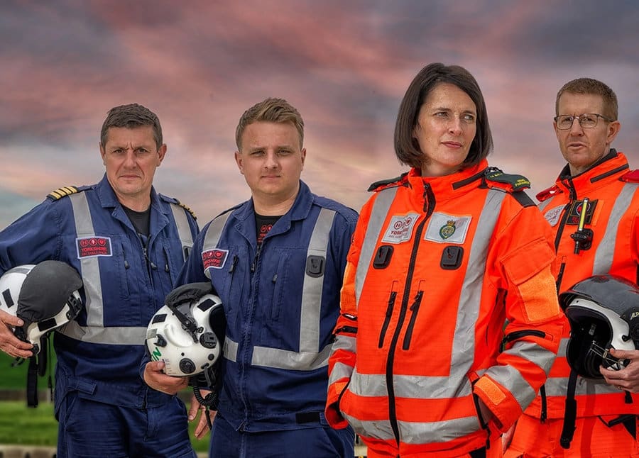 Four Yorkshire Air Ambulance crew members in flight suits, holding their helmets